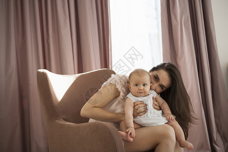 母亲座在扶手椅上和婴儿玩耍图片