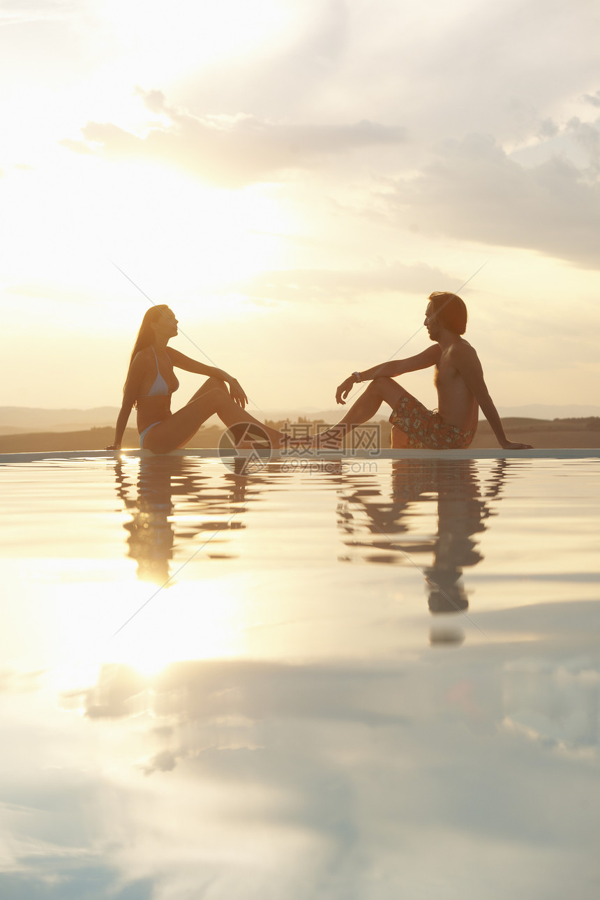 阳光下坐在无限游泳池边的一对夫妇图片