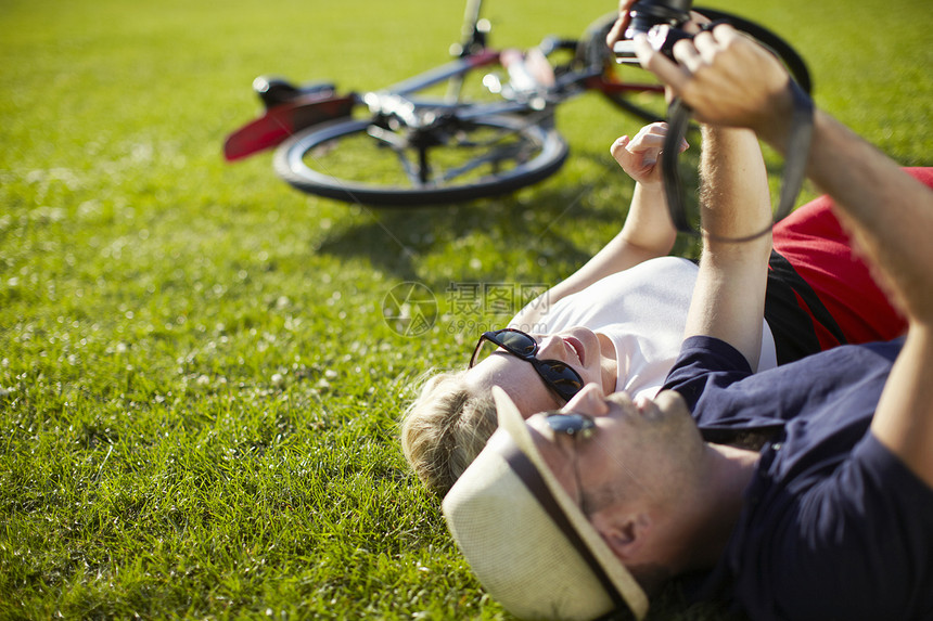躺在公园草坪上使用数码相机照相的夫妇图片