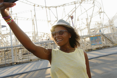在游乐园使用智能手机自拍的年轻女性图片