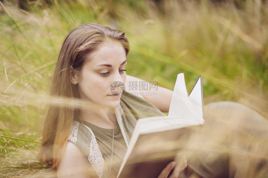 坐在长草丛读书的年轻妇女图片