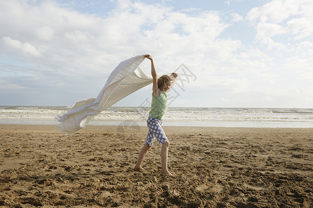 微风习习的海滩上一个女孩拿着毯子走支撑高清图片素材
