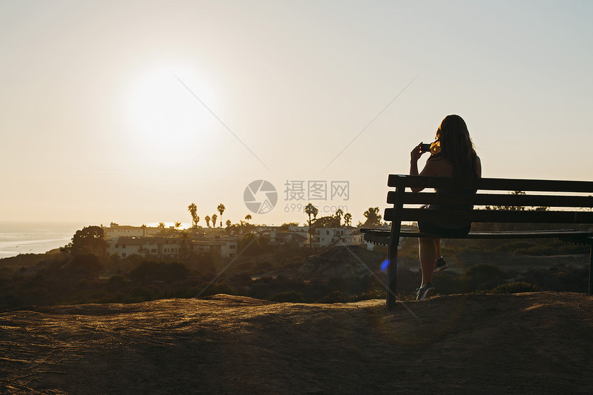 坐在山顶的长椅上拍摄照片的年轻女子图片