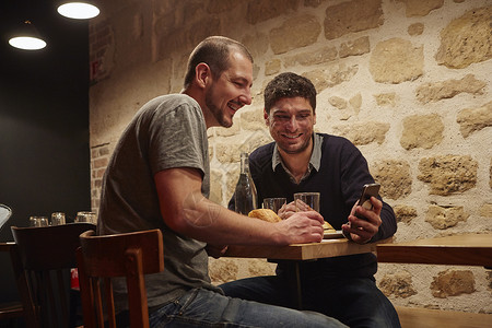 在餐厅一个男人向另一个人展示他的智能手机图片