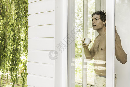 光着胸脯的年轻人喝着咖啡从窗户往外看背景图片