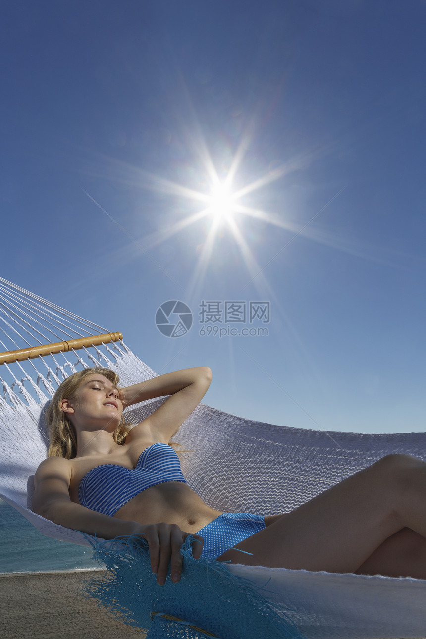 阳光照耀的海滩上年轻女人躺在吊床上图片