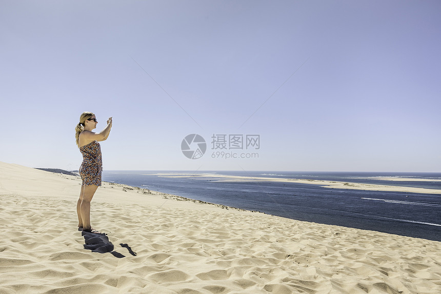 女青年用智能手机在海滩拍照图片