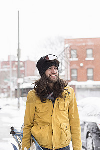 在雪覆盖的街道上微笑的男滑雪运动员图片