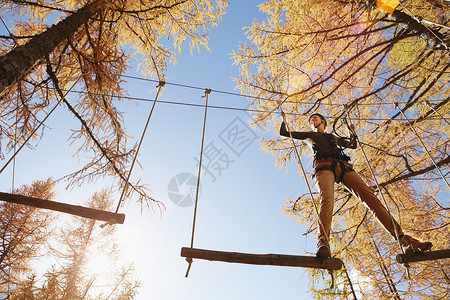 成年女子在森林中攀爬附着高绳低角度视图片