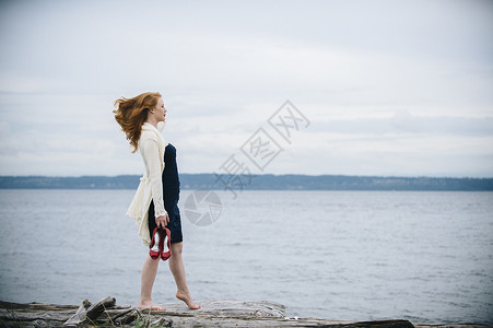 拎着高跟鞋在海边走路的女子图片