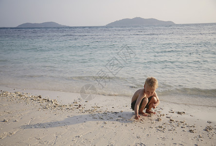 马来西亚拉瓦岛沙滩上玩沙子的男孩童年高清图片素材