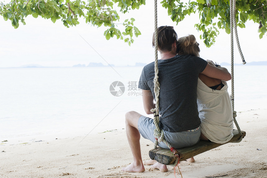 坐在泰国克拉丹海滩摇摆上的年轻夫妇后视景图片