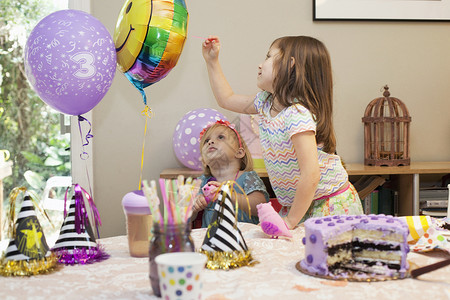 两个女孩坐在生日派对桌边蛋糕玩气球背景图片