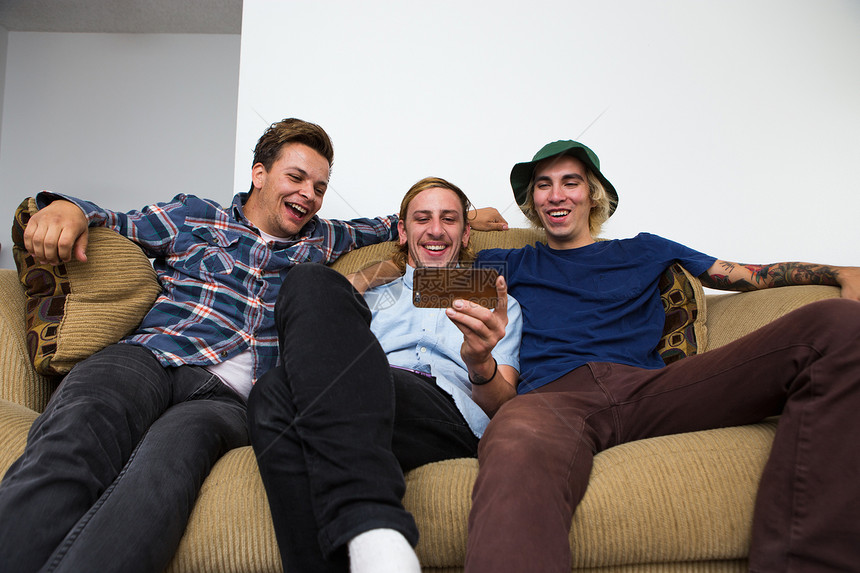 三个年轻人坐在沙发上玩手机图片