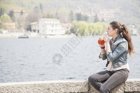 年轻女子坐在湖边喝鸡尾酒高清图片