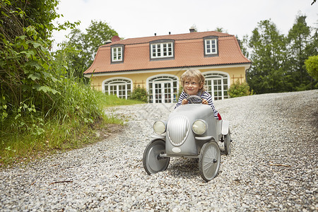 男孩在房子前面的路上玩儿童车背景图片