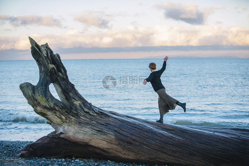 妇女站在沙滩上大型漂木树干图片