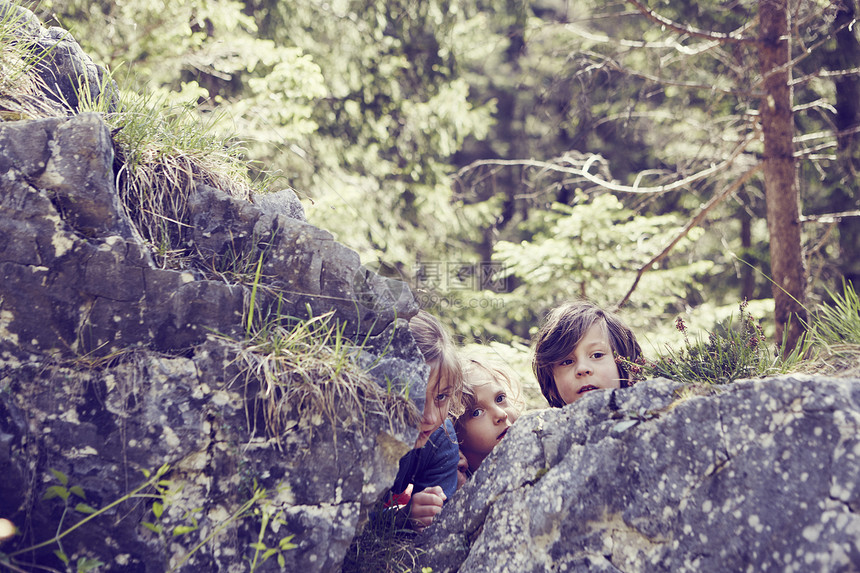 三名儿童躲在森林中的岩石后面图片