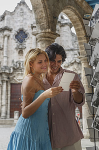 在古巴哈瓦那大教堂广场看明信片的年轻夫妇图片