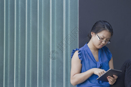 使用数字平板电脑触摸屏在墙前的年轻妇女图片