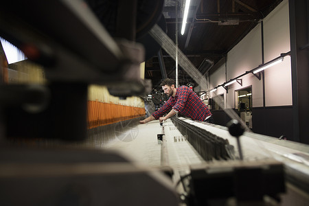 年轻的男织工在纺织厂的旧织机上工作图片