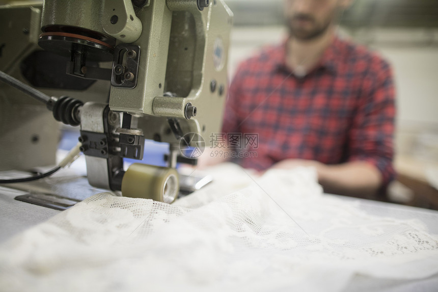 在旧纺织厂缝纫机上编织蕾丝的年轻男性图片