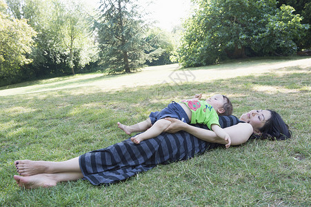 母亲抱着儿子躺在草在公园地上童年高清图片素材
