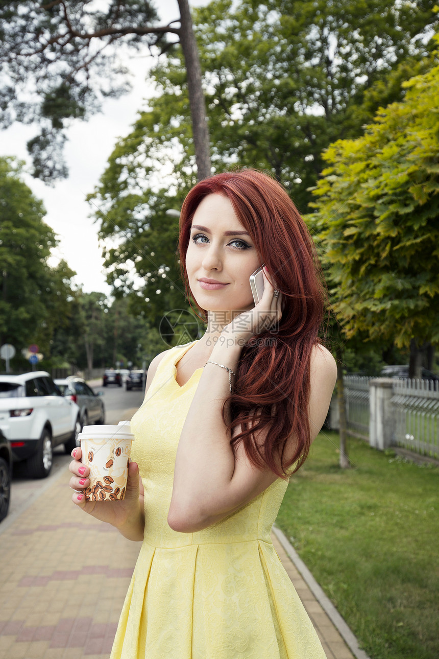 在街上端着咖啡杯打电话的女青年图片