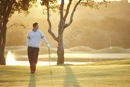 夕阳下的高尔夫球手手放在口袋里向远处看图片