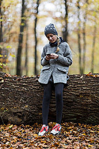 秋森林树干上使用智能手机的女孩图片