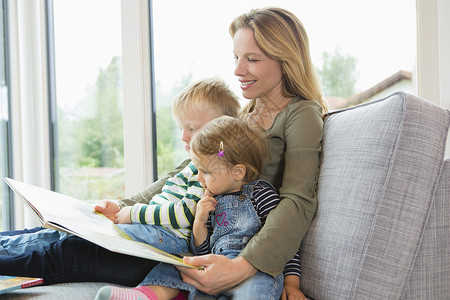 母亲和两个小孩坐在沙发上看书图片