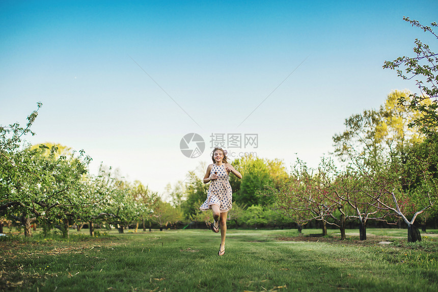 穿着无袖服装的年轻女子在果园中跑动看着镜头微笑的全长前视线图片