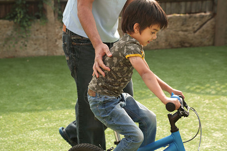 父亲帮助男孩学习骑自行车图片