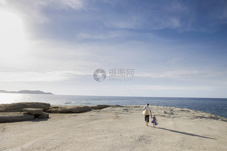 男人和他蹒跚学步的女儿在海滩上散步图片