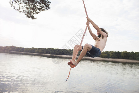 年轻人抓着绳子在湖上摇摆图片