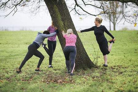 妇女和少年在公园树周围做温暖运动图片