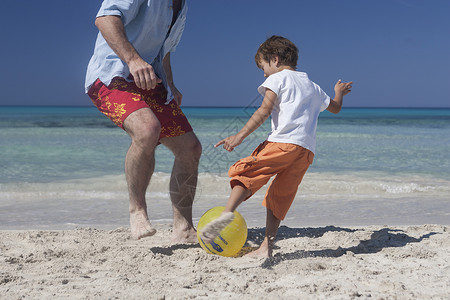 男孩与父亲在西班牙马杰卡海滩踢球图片