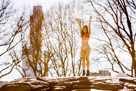 身穿比基尼的年轻女子站在冬季公园的岩石上纽约高清图片素材