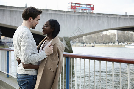 站在河边的一对情侣面对面男人把外套在女的肩膀上图片