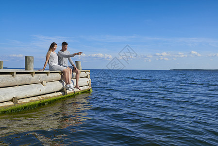 年轻夫妇坐在木码头上看海聊天图片
