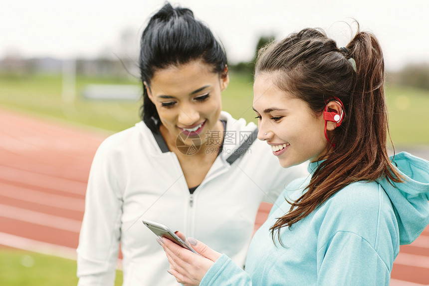 两个年轻女子在赛跑道旁看着智能手机图片