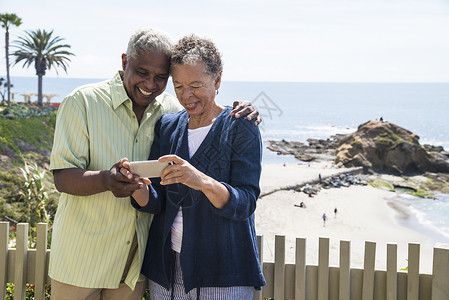 高龄夫妇站在海滩旁边看着智能手机自由高清图片素材