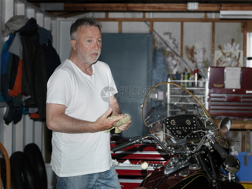 老年男子在车库清洗摩托时擦手图片