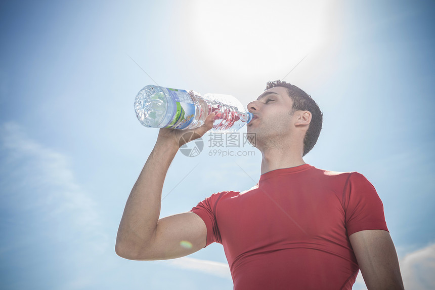 青年男子饮用瓶装水对抗蓝天图片