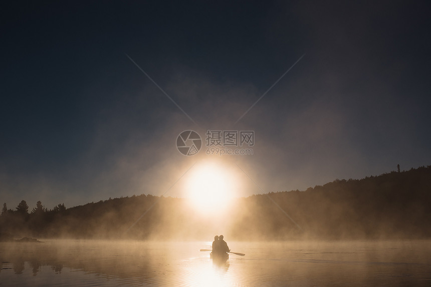 日落时在湖上搭乘独木舟的夫妇图片