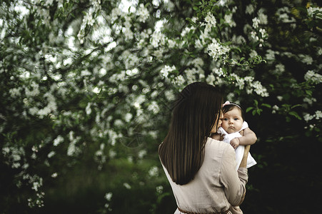 在花园苹果树旁亲吻女婴的妇女图片