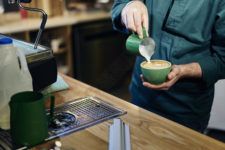 在咖啡店将牛奶倒入咖啡厅杯的男服务员图片