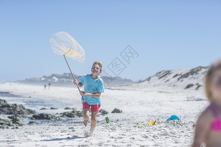 背着渔网的男孩男孩在南非开普敦带渔网在海滩上奔跑背景