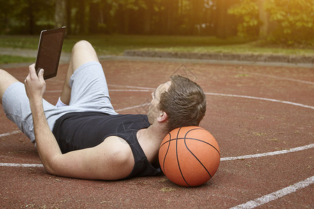 年轻男篮球运动员躺在场地上看平板电脑图片