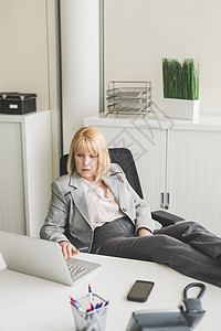 在办公桌上翘着脚的女人使用电脑图片